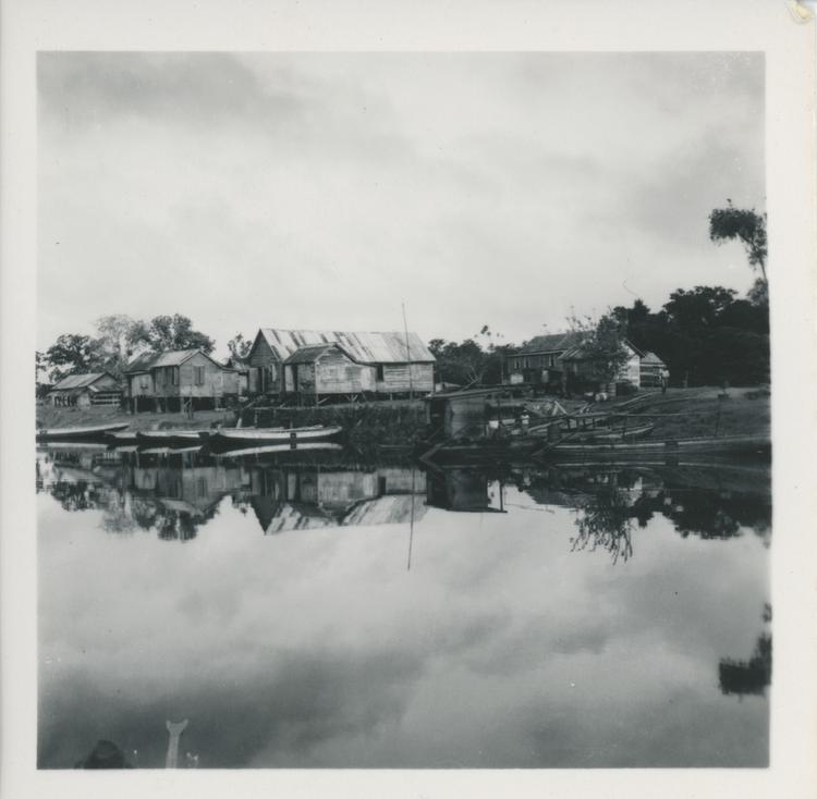 Black and white print of houses and boats seen from river with clear reflection