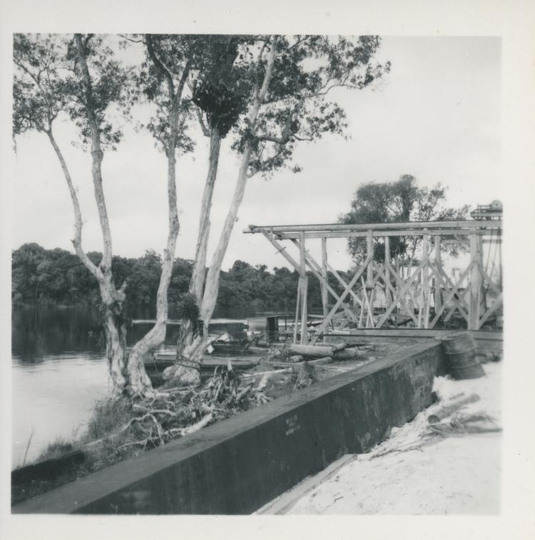 Black and white print of trees and wood structure next to river