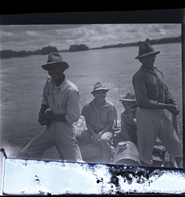 image of Black and white medium format negative of four men in a boat (with motor) with river behind