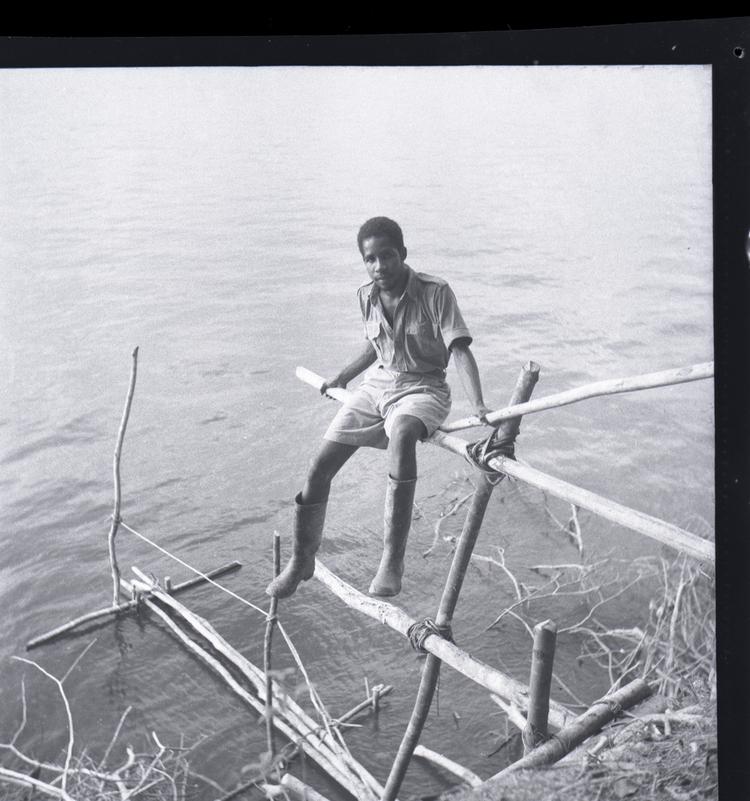 Black and white medium format negative of young man sitting on landing stage