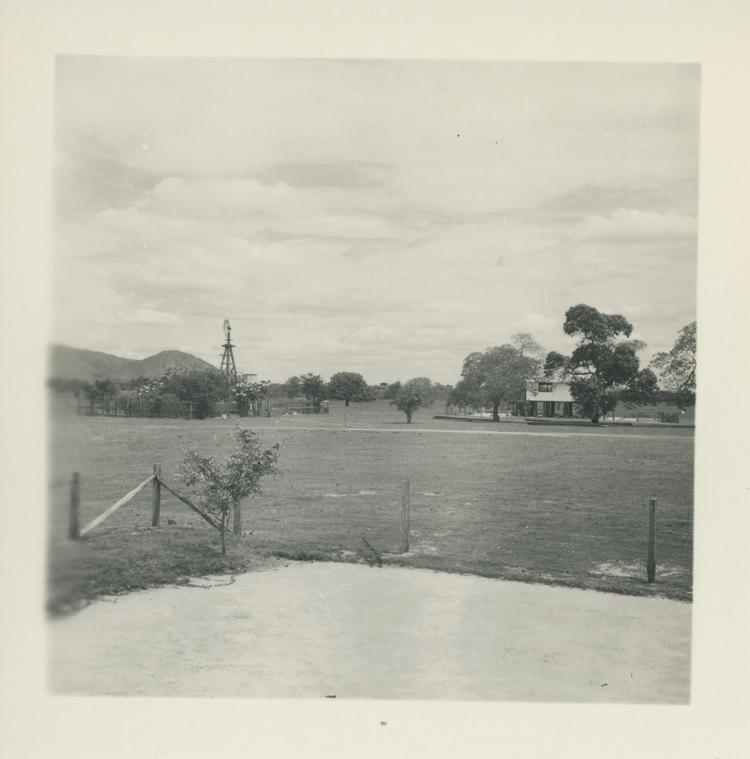 Image of Black and white print of building in distance among trees - possibly a pond in the foreground