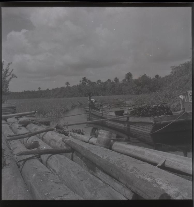 image of Black and white medium format negative of with logs in foreground and loaded boat on river