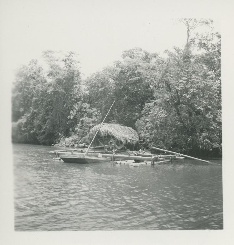 image of Black and white print of raft with thatched roof and logs at side of river