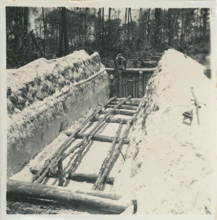 Image of Black and white print of a man made pit with a few logs at the bottom