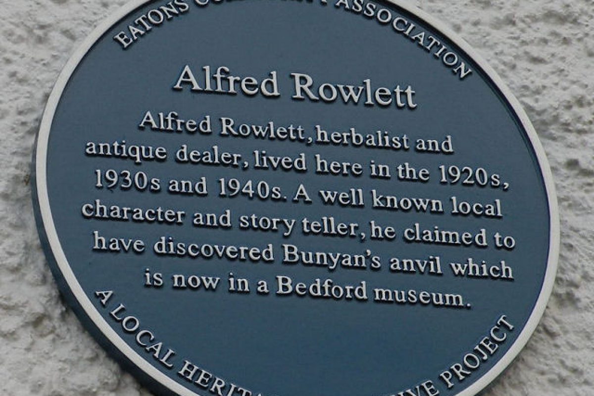 A blue plaque on a white wall about Alfred Rowlett