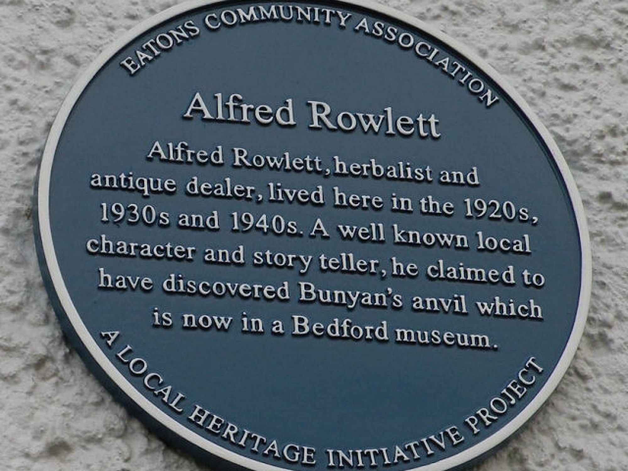 A blue plaque on a white wall about Alfred Rowlett