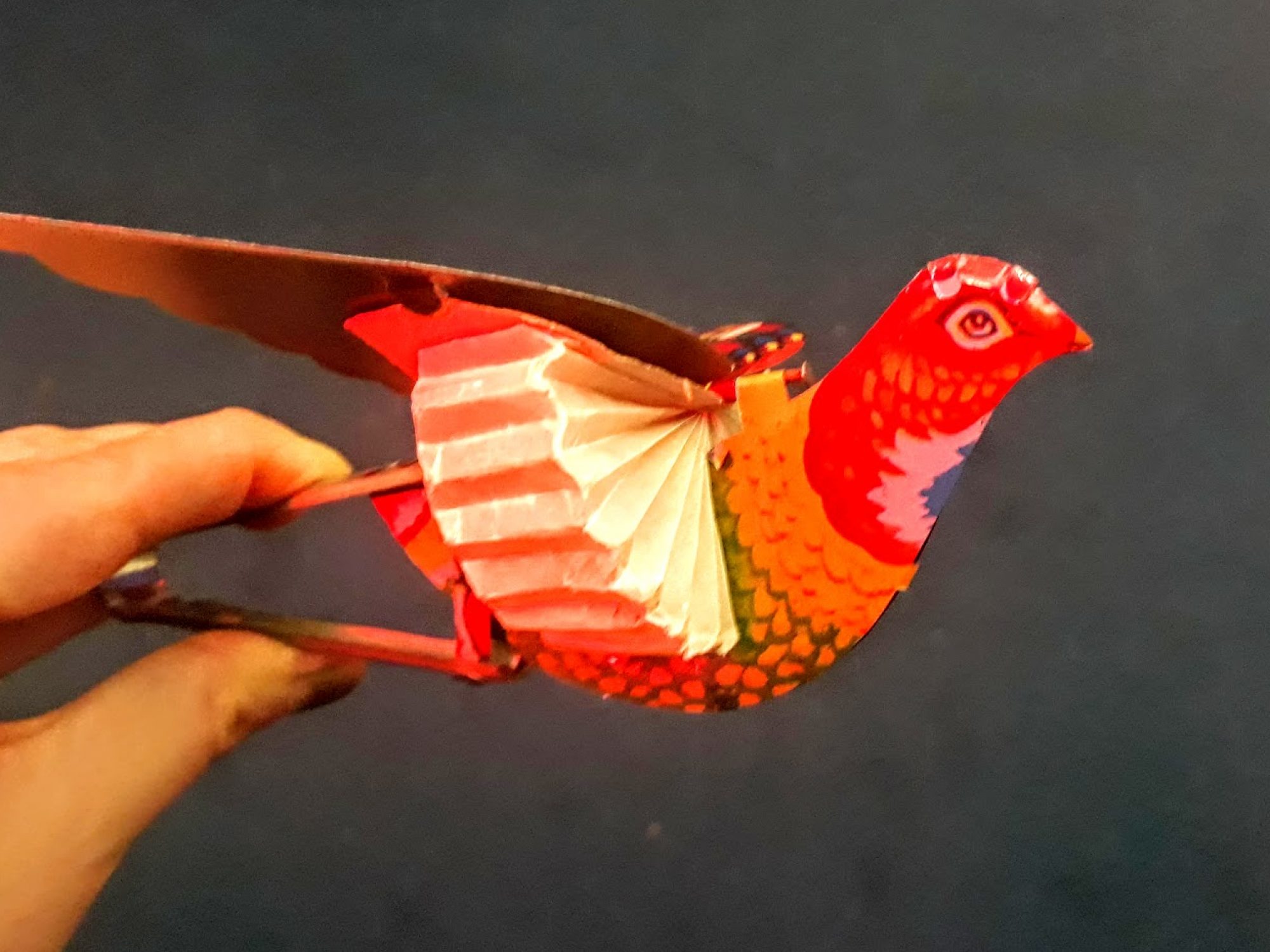 Two images, one on top of the other of a paper red bird with wings which open