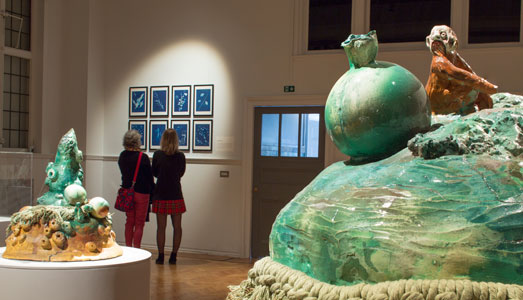 Two women looking at images on wall. Blue sculpture in foreground.