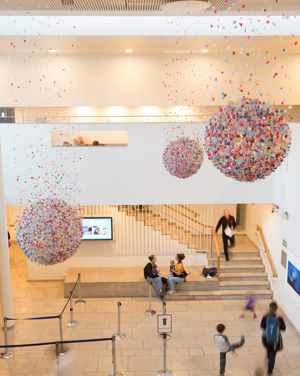 Three spheres suspended from ceiling. People walking around gallery