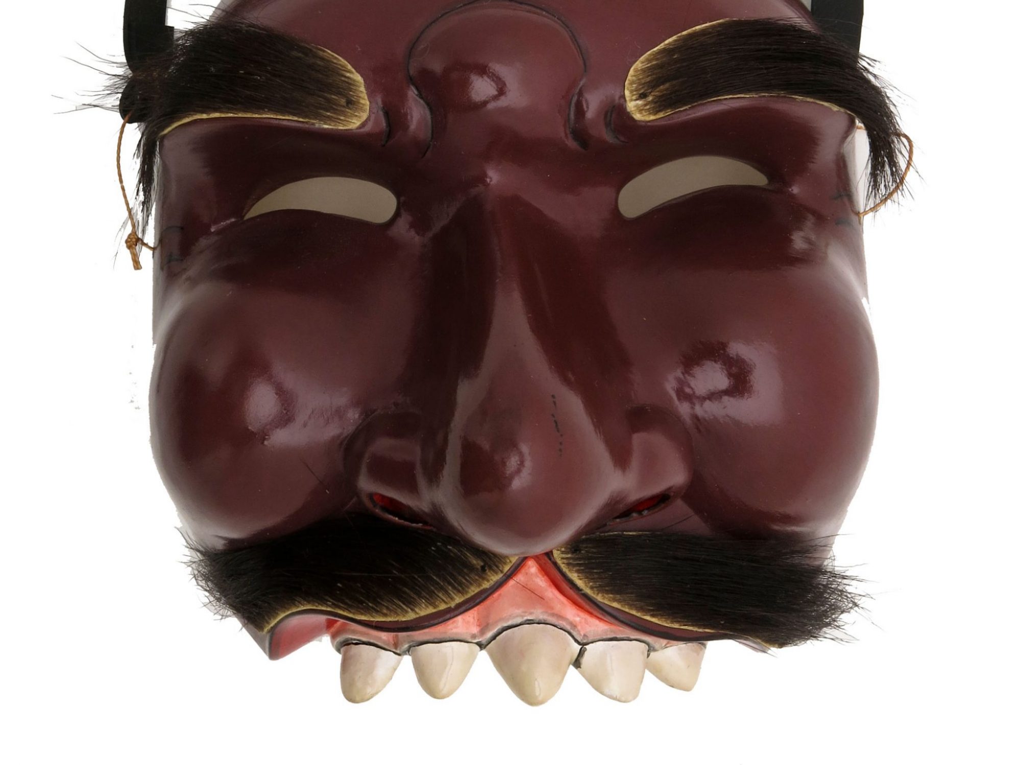 Carved wooden half mask of Cungih with face painted brown, cleft lip and palate. No lower jaw. Narrow curved apertures for eyes. Moustache and eyebrows are made of animal skin and hair. Secured when worn by a band of black rubber is tied with string which passes through a hole in each side of the mask.