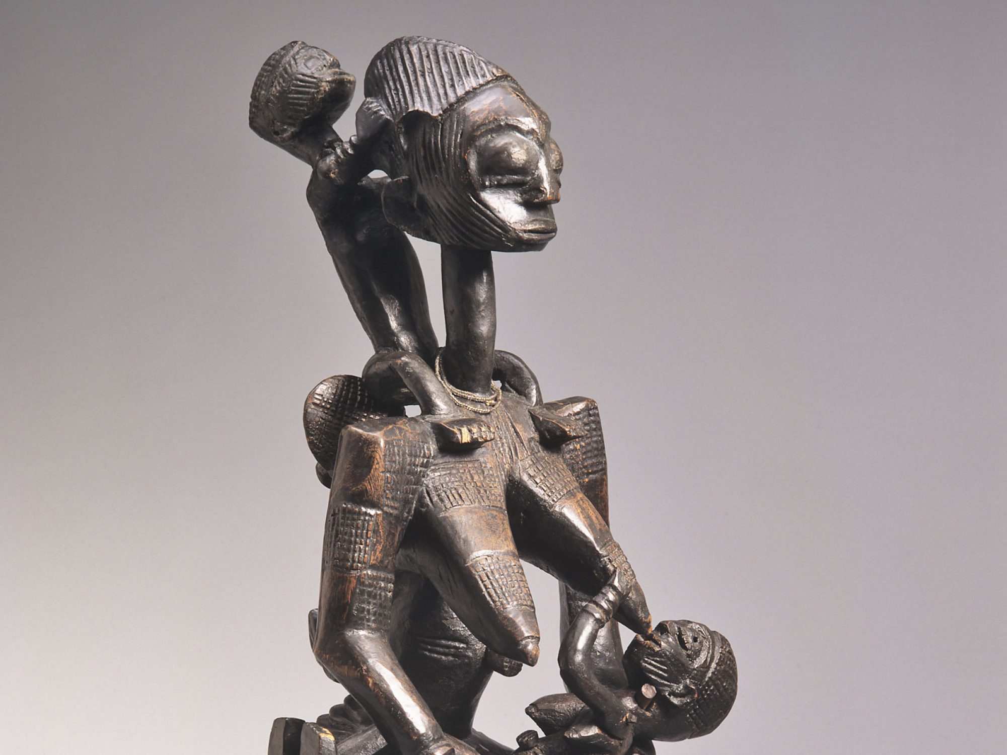 Afo figure, 'ngorongoro'. Seated wooden female suckling a child, with two more on her back.