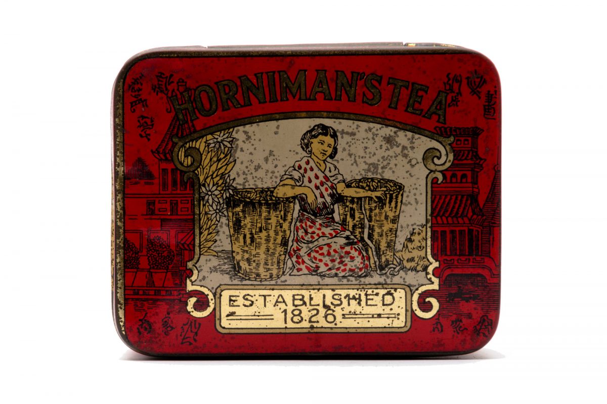 An old mottled tea tin with the words Hornimans Tea on it and a picture of a woman. The tin is red and gold.