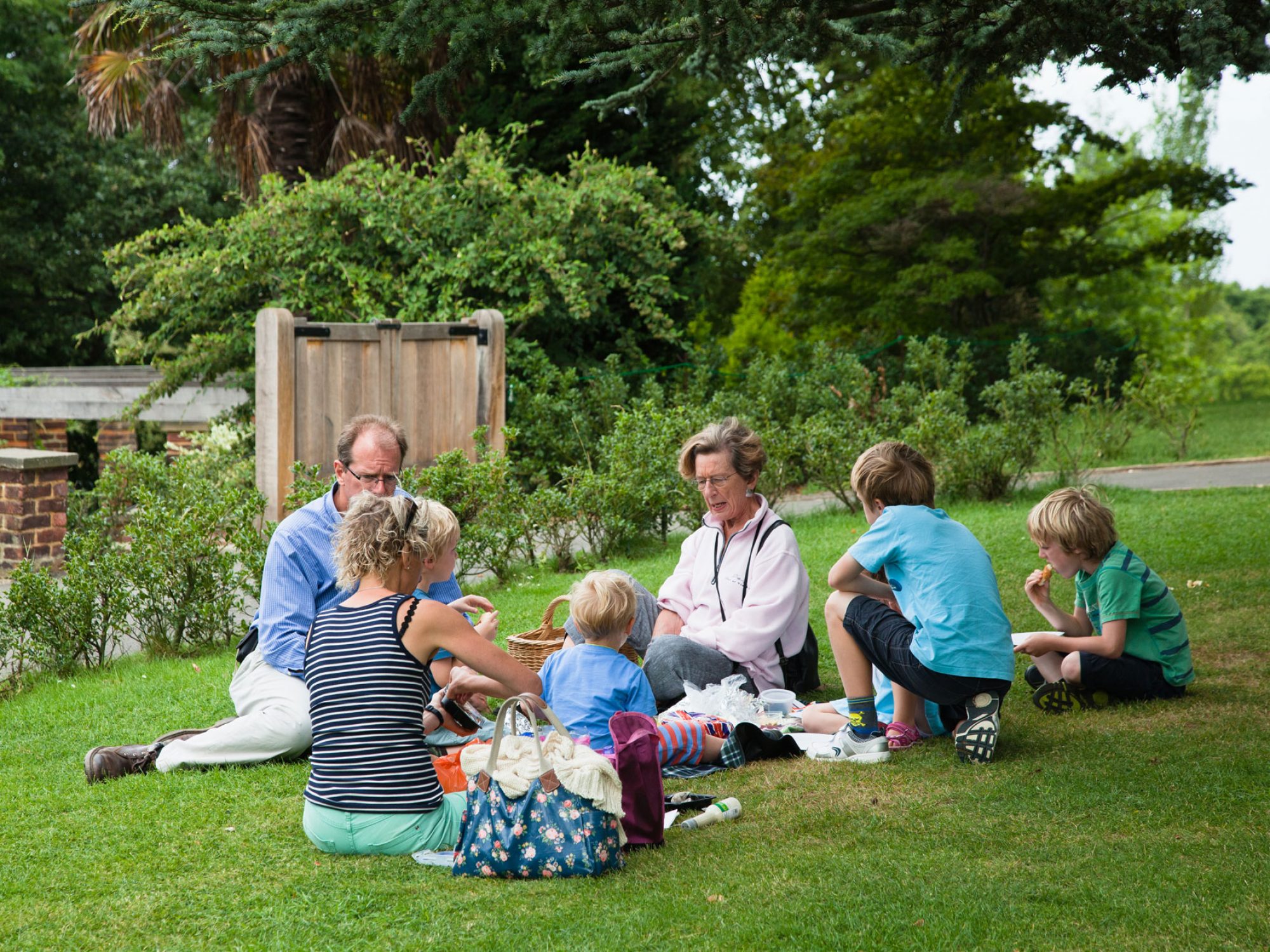 A family with parents children and grandparents are eating a picnic in a Garden