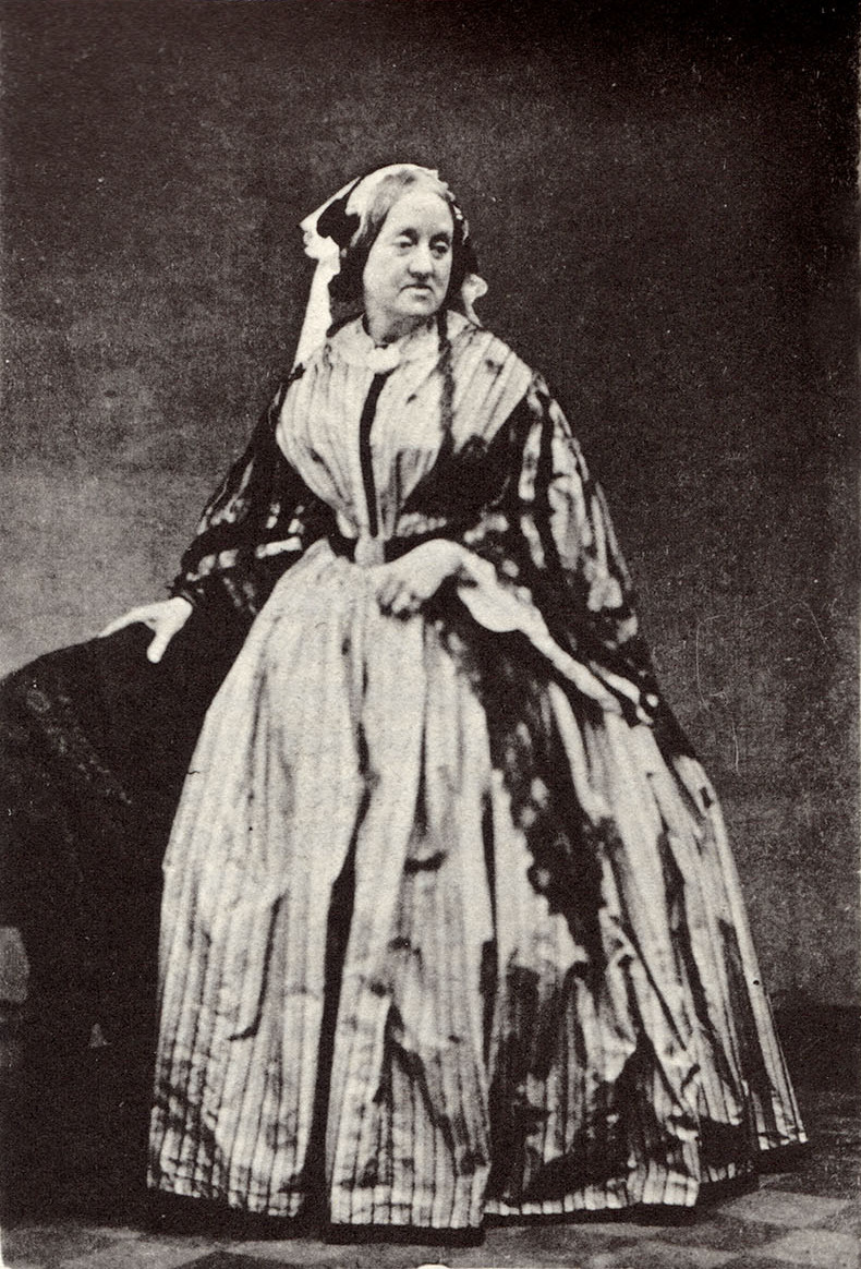 A black and white portrait of a woman in a full Victorian outfit