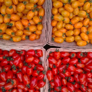 Four baskets with yellow baby tomatoes in the top two and red baby tomatoes in the bottom one
