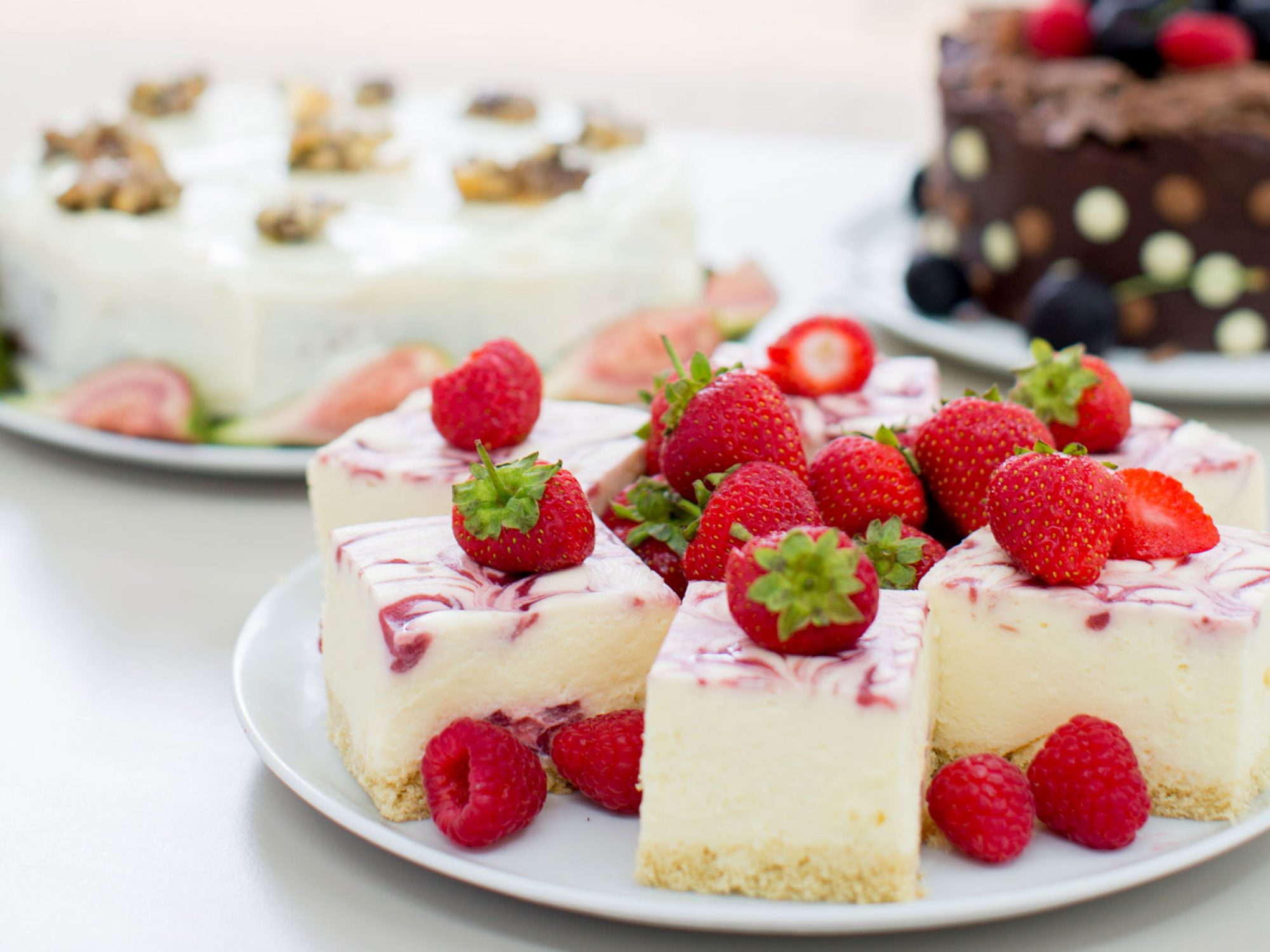 Three cakes on a table in an outdoor setting. One cake has strawberries on it and one is chocolate. The other looks like walnuts are on top.