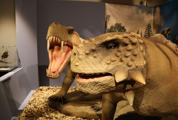 Two prehistoric creatures with large teeth and face spikes. One has its mouth open in a roar. They are animatronix figures