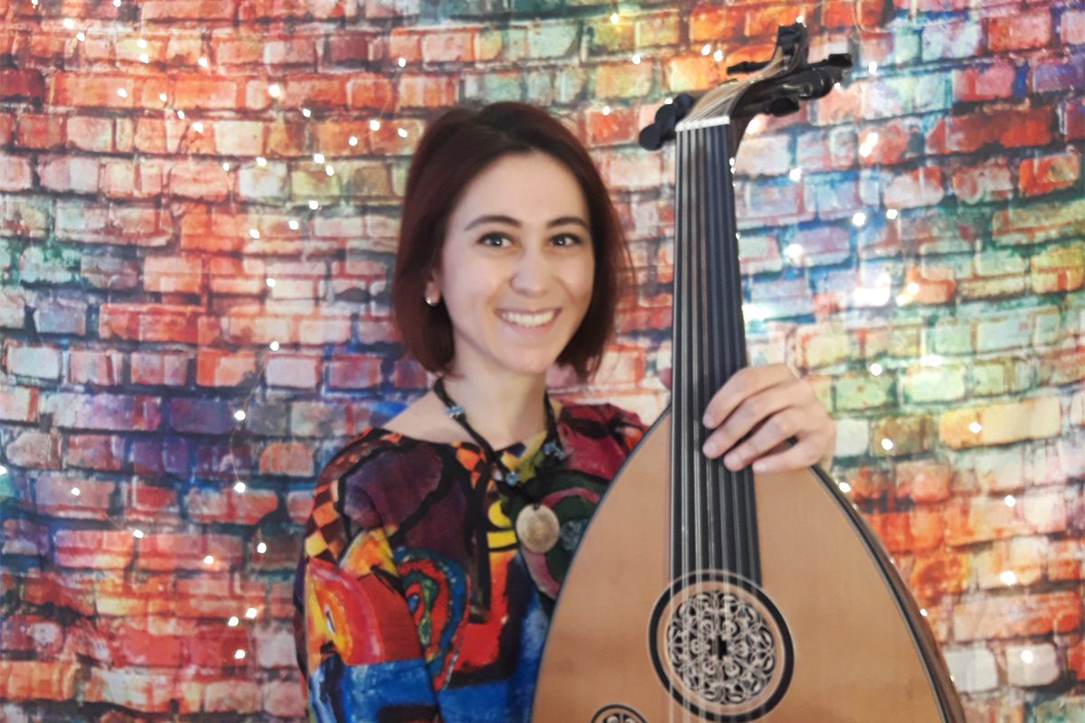 Musician Rihab Azar holds a Syrian oud and stands against a colourful wall