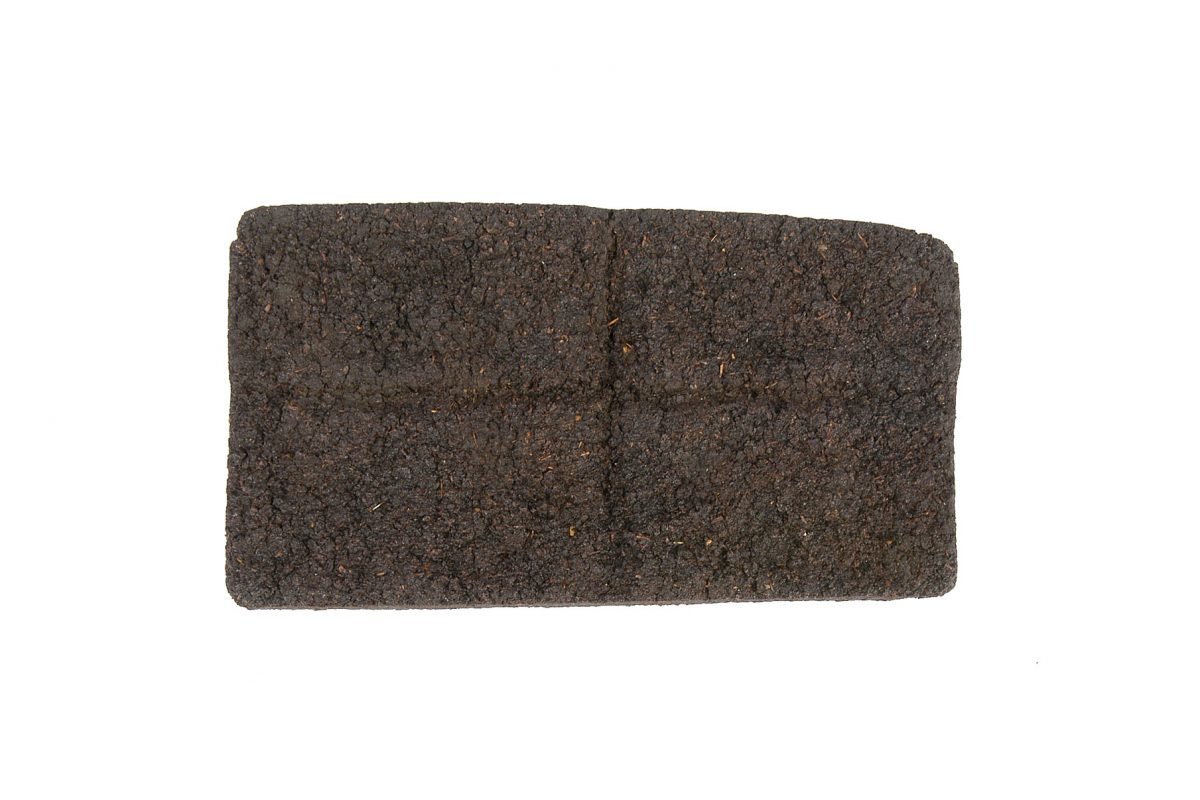 A brown brick shaped object made of a dense looking brown material, with a cross in the centre, so that it can be split into four smaller blocks