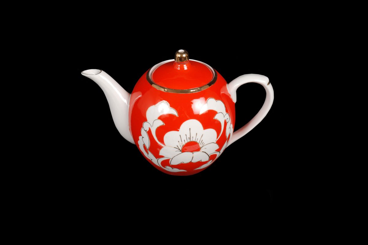 Teapot and lid. Part of a factory made pottery tea set. Typical decoration with white motifs (cotton plants) on an orange-red ground, trimmed with a golden band around the rim. The teapot has a globular form.