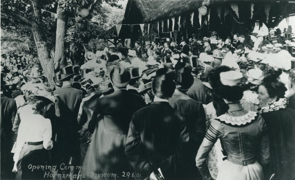 black and white photograph of men and women in stylish Edwardian dress, like top hats and gowns. They are outside in a Garden