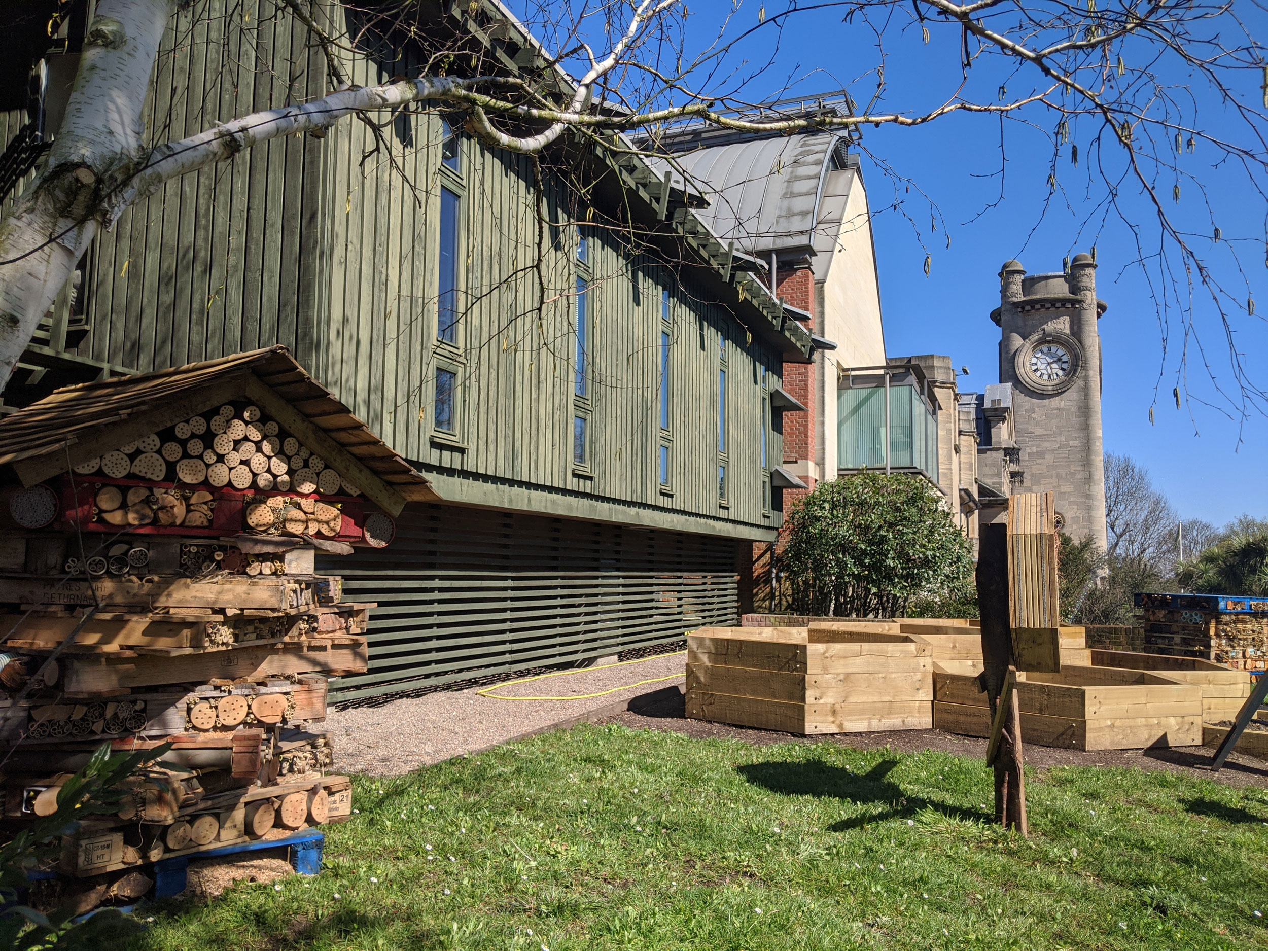 A small lawn in front of the Horniman buildings with wooden short planters and loose wooden houses made of bamboo and palettes to create bee houses