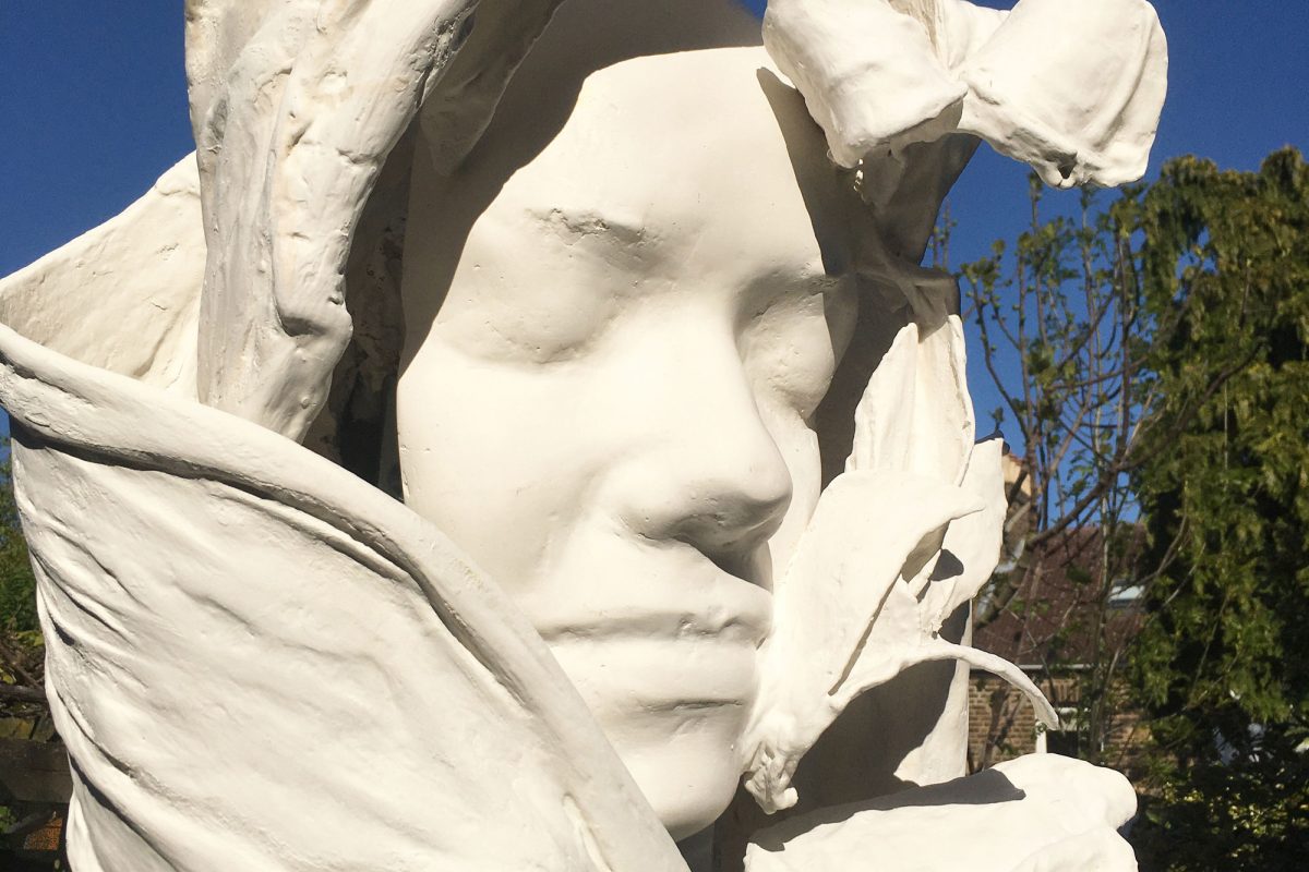 A sculpture of a woman's face surrounded by white petals or swathes of fabric