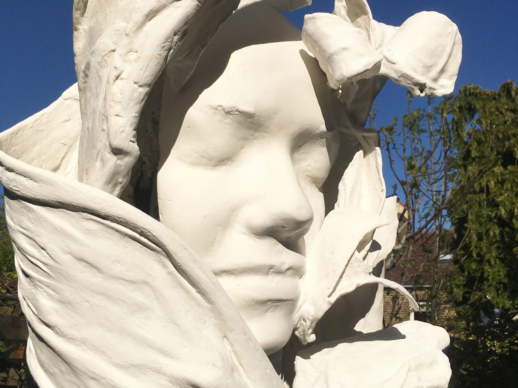 A sculpture of a woman's face surrounded by white petals or swathes of fabric