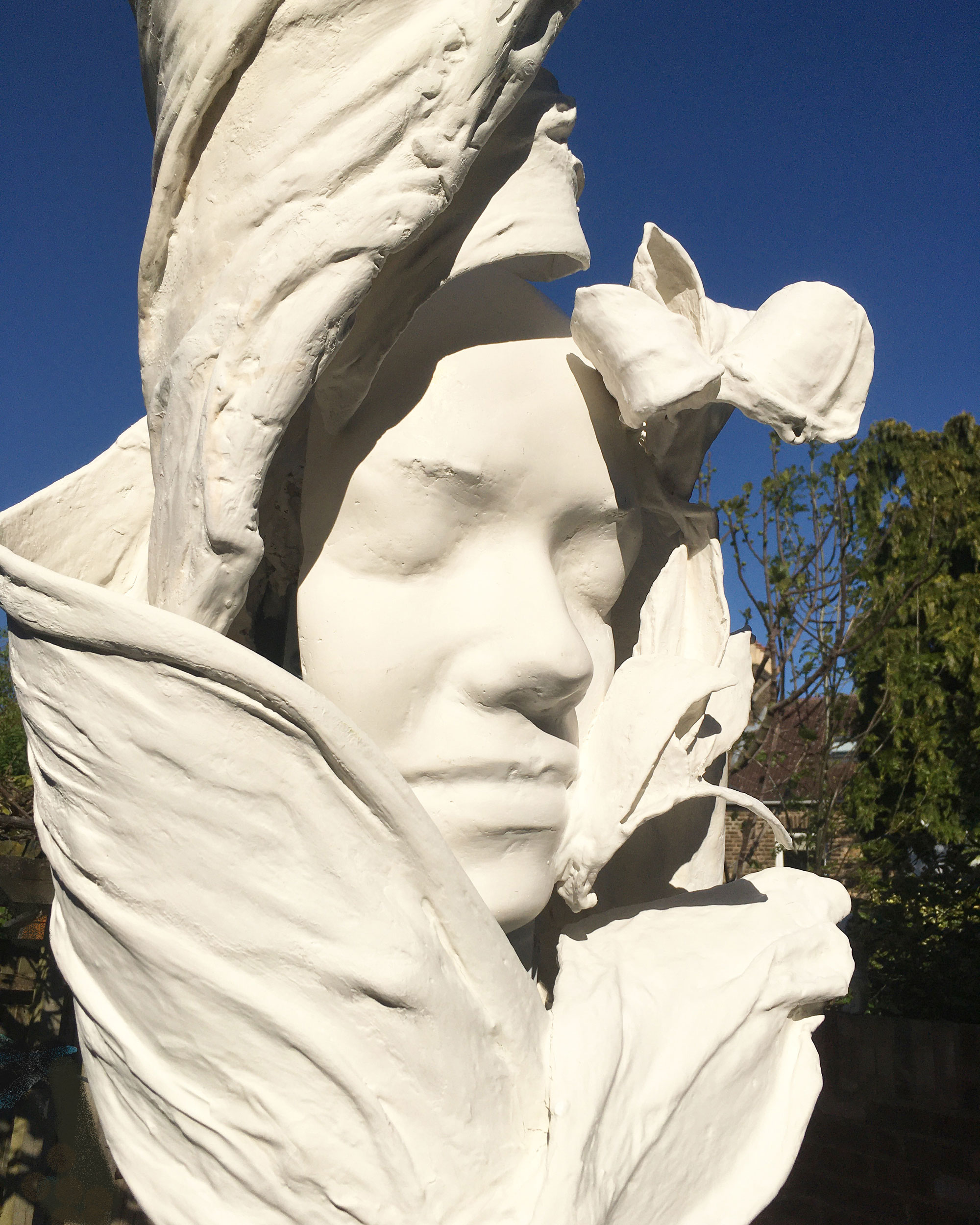 A sculpture of a woman's face surrounded by white petals or swathes of fabric