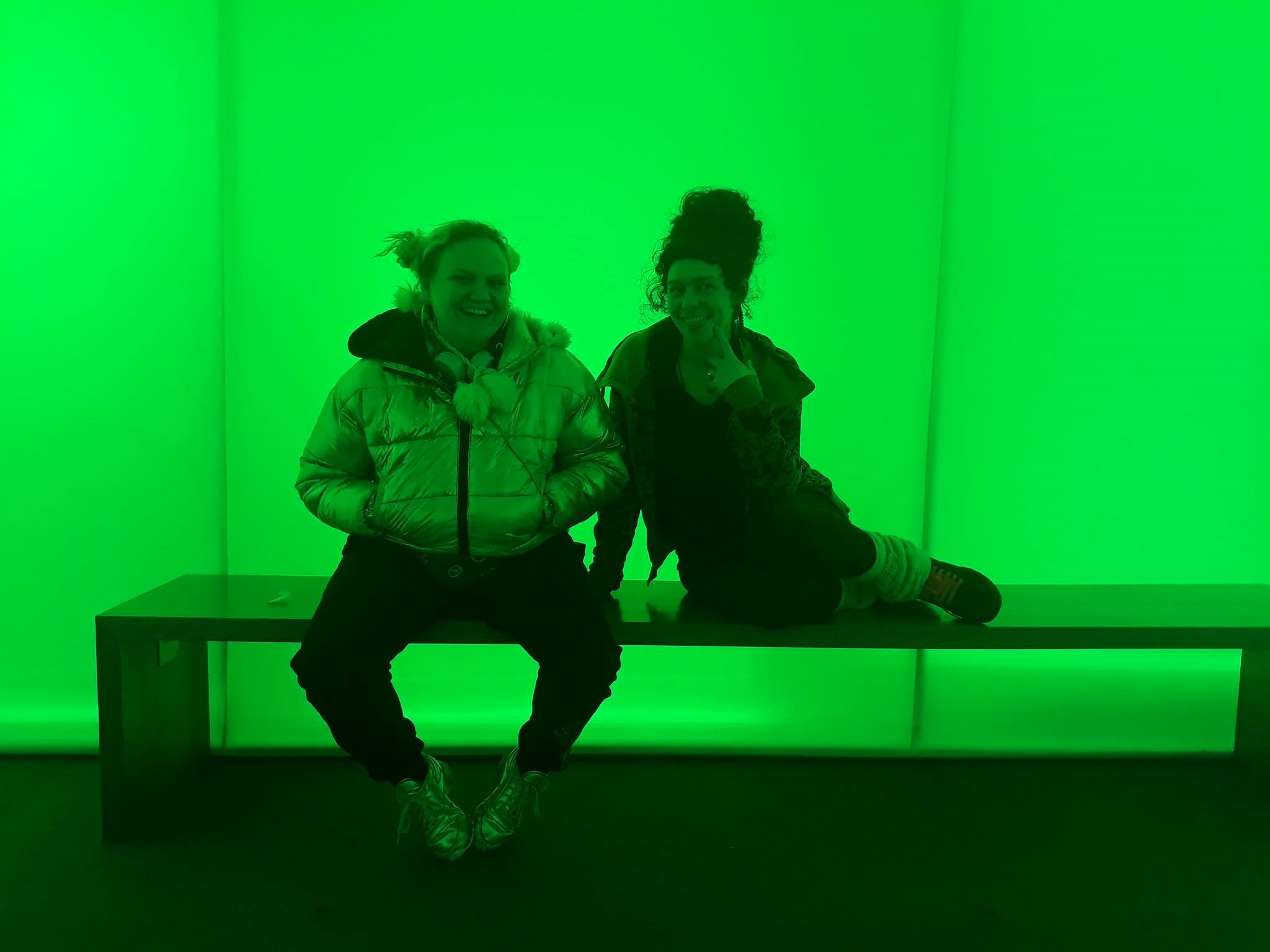Two female teenagers sitting on bench in green lit room