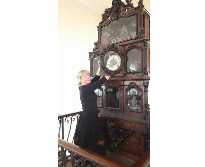 Female visitor host standing next to apostle clock