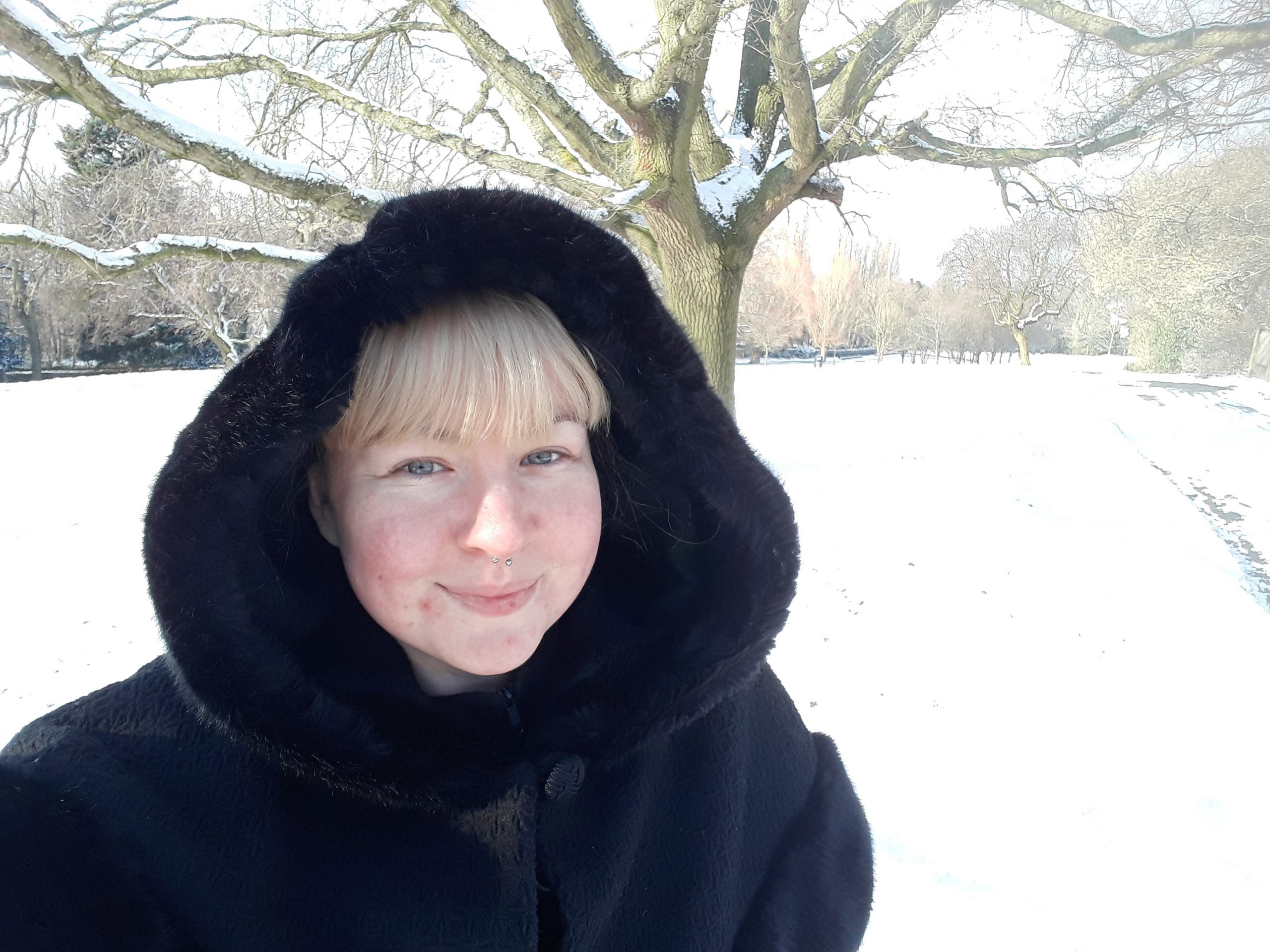 Female in black fax fur coat standing gardens filled with snow.