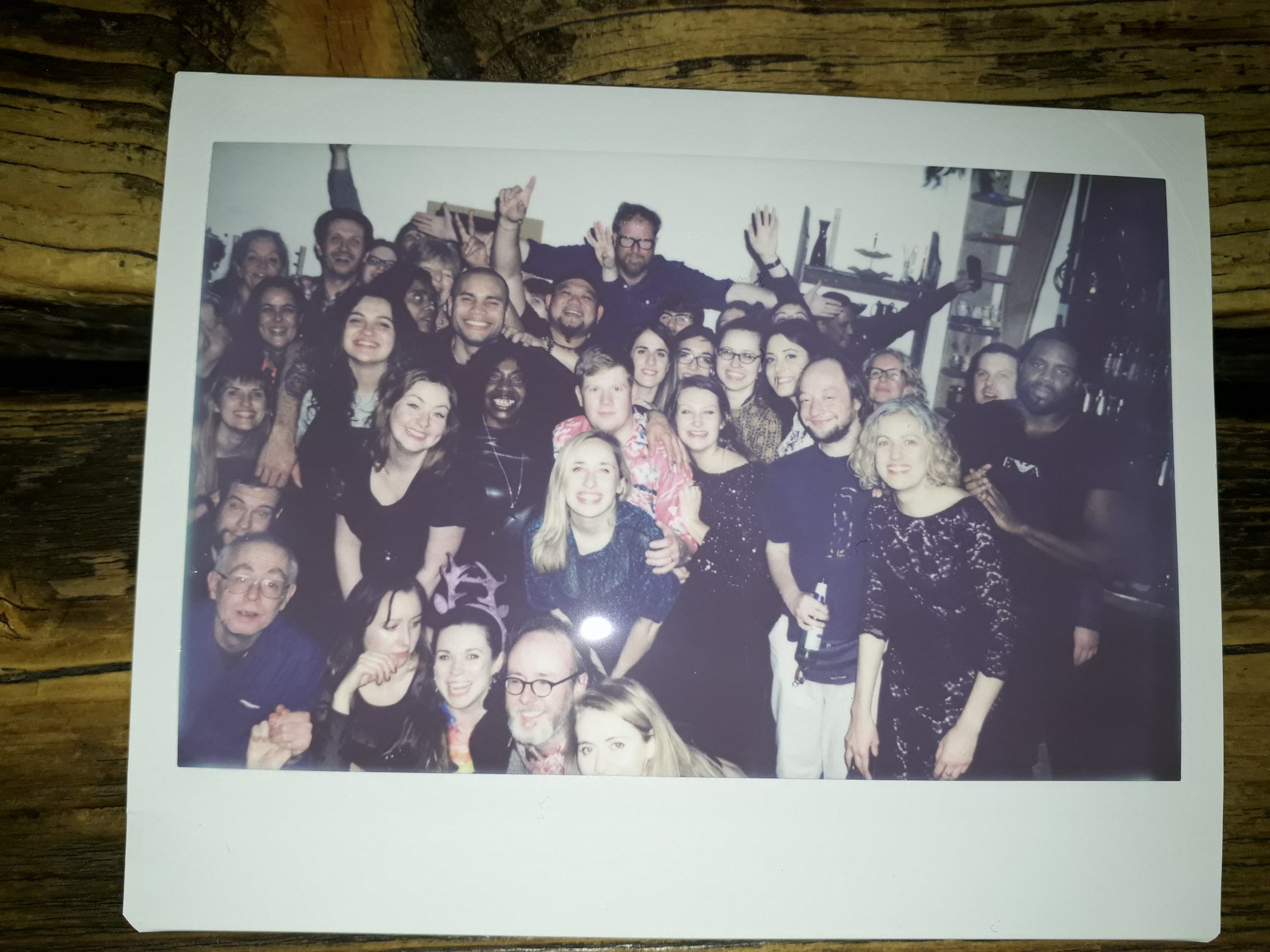 A Polaroid with a large group of men and women gathered together smiling