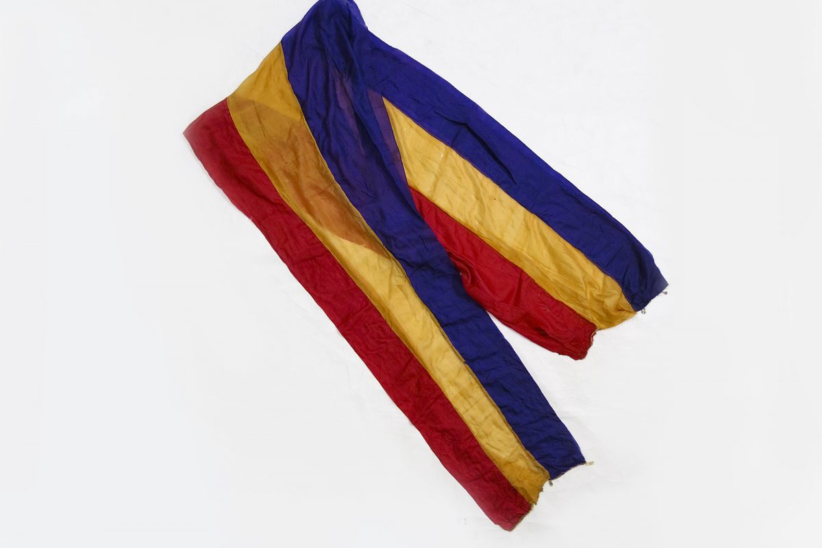 A piece of light fabric with three stripes of colours, red, yellow and blue.