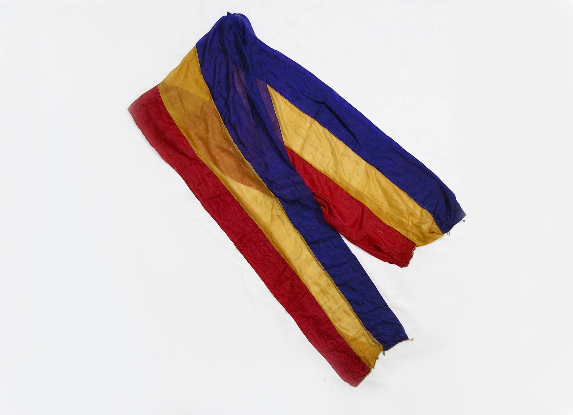 A piece of light fabric with three stripes of colours, red, yellow and blue.