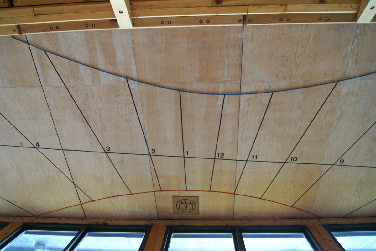 A sundial on a wooden ceiling with windows below