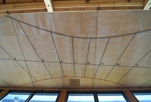 A sundial on a wooden ceiling with windows below