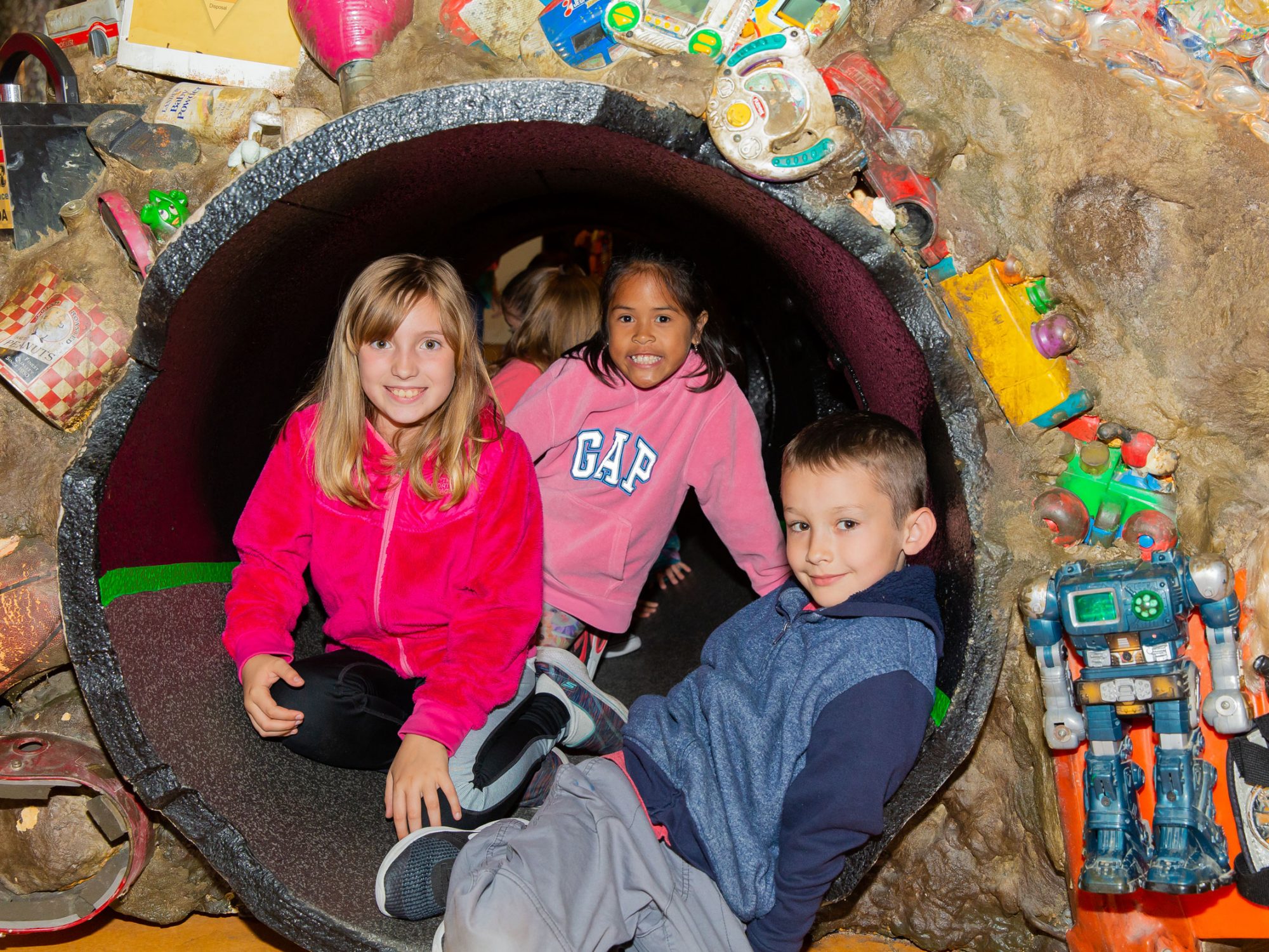 Children sitting in a tunnel through a fake trash pile