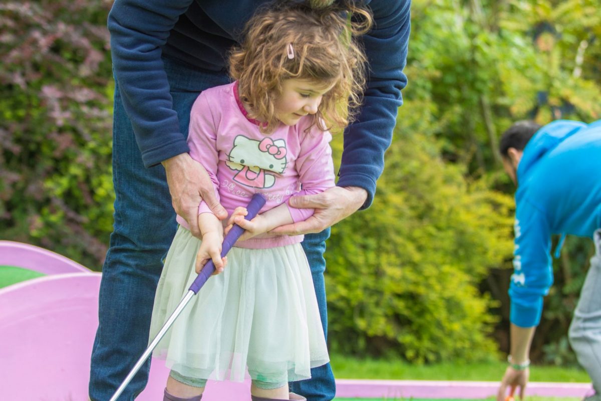 A man helps a young girl on a golf hole