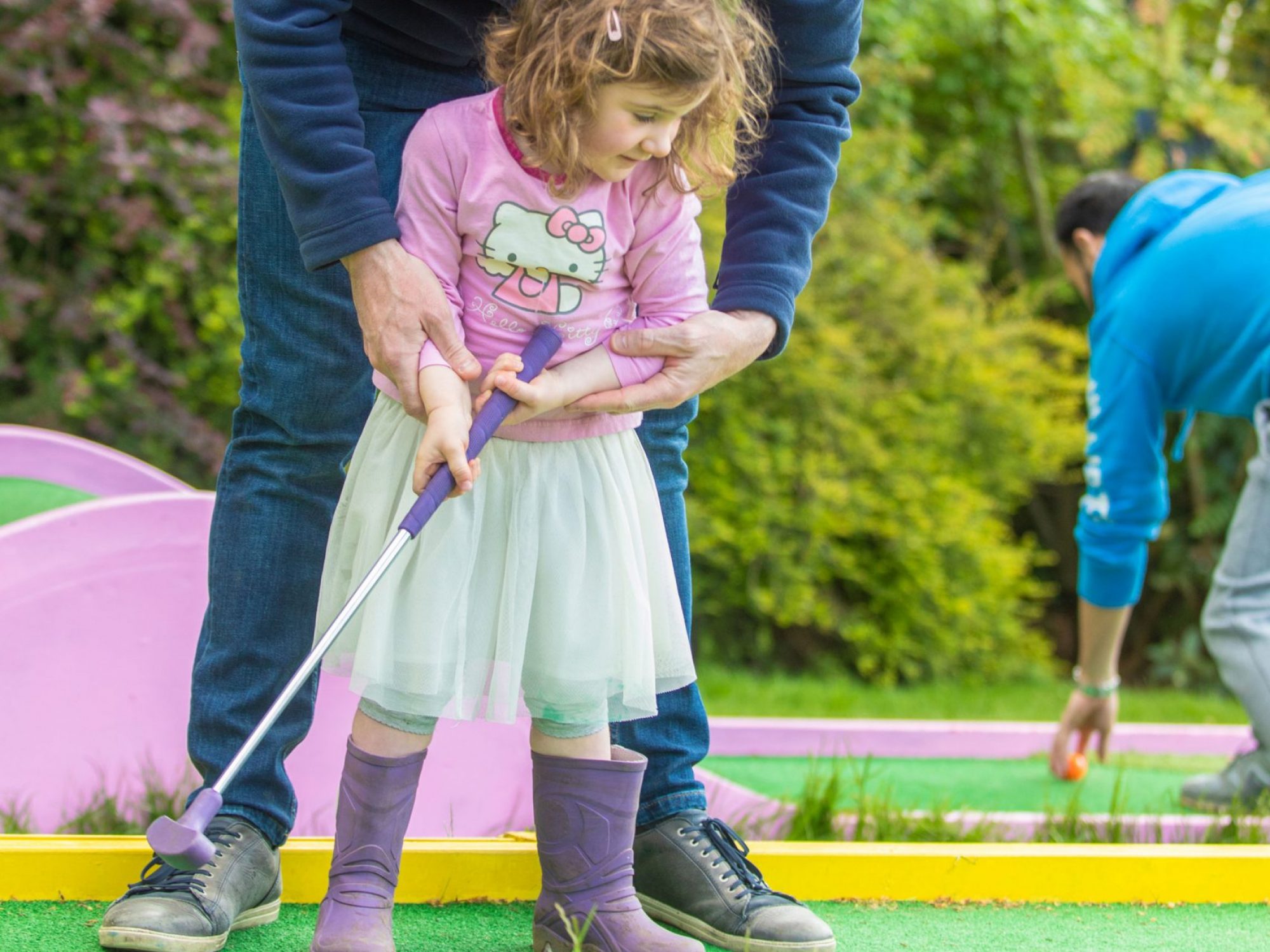 A man helps a young girl on a golf hole