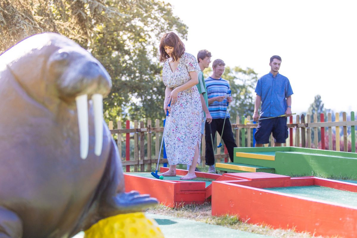 A group of young adults plays on a golf course next to a large walrus statue