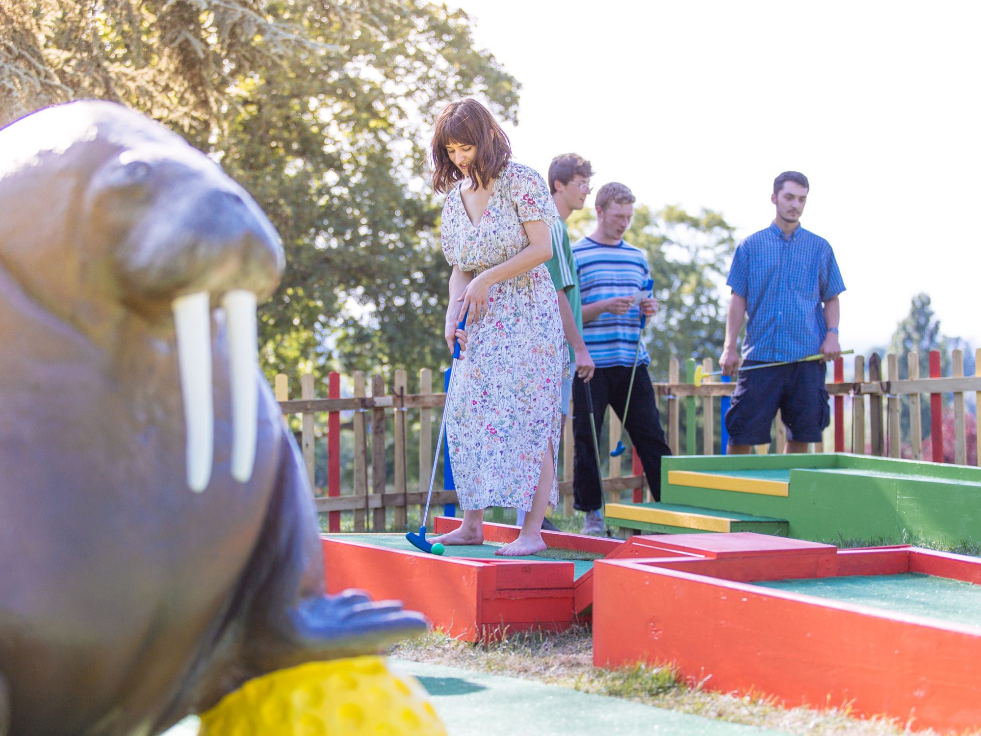 A group of young adults plays on a golf course next to a large walrus statue