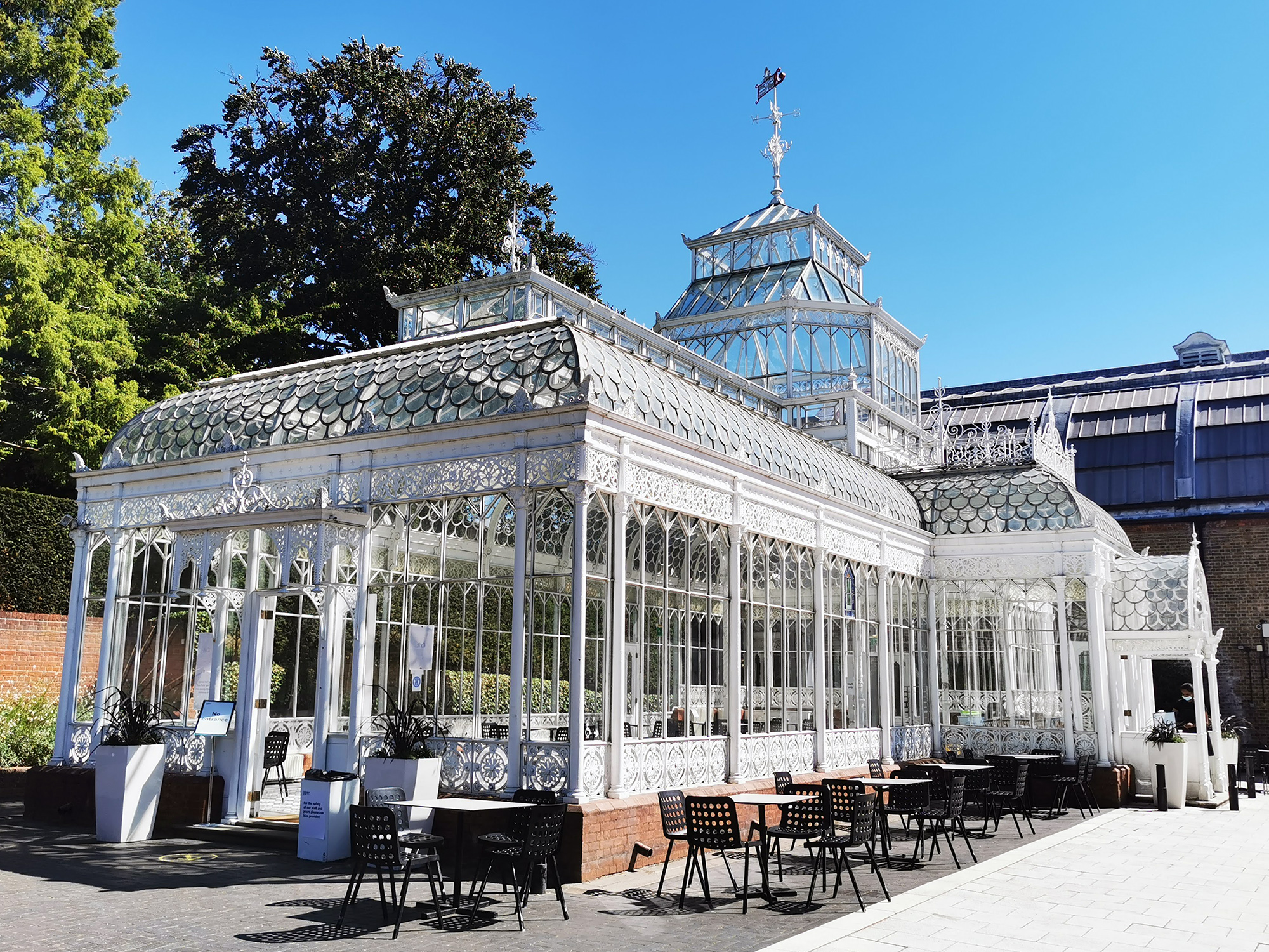 Glass building with seating and tables outside. Clear sunny day.