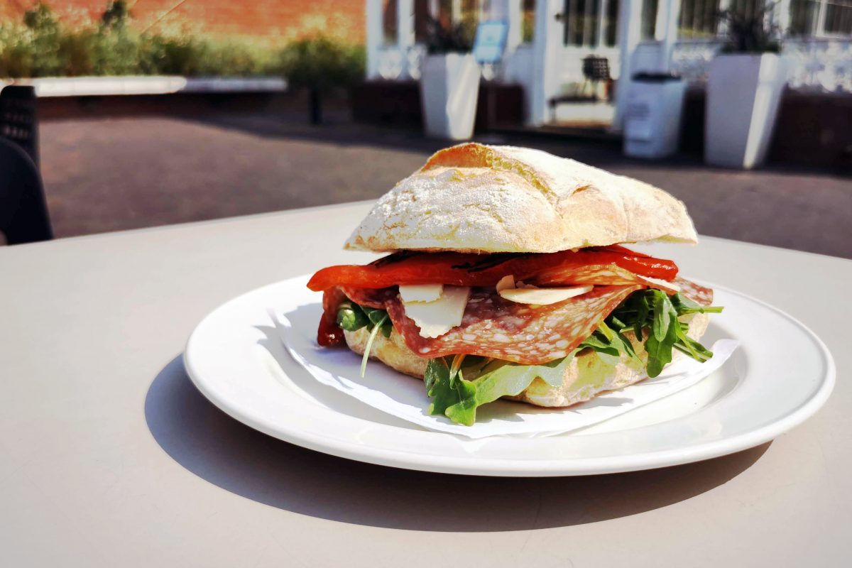 large sandwhich on a plate and table near glass building.