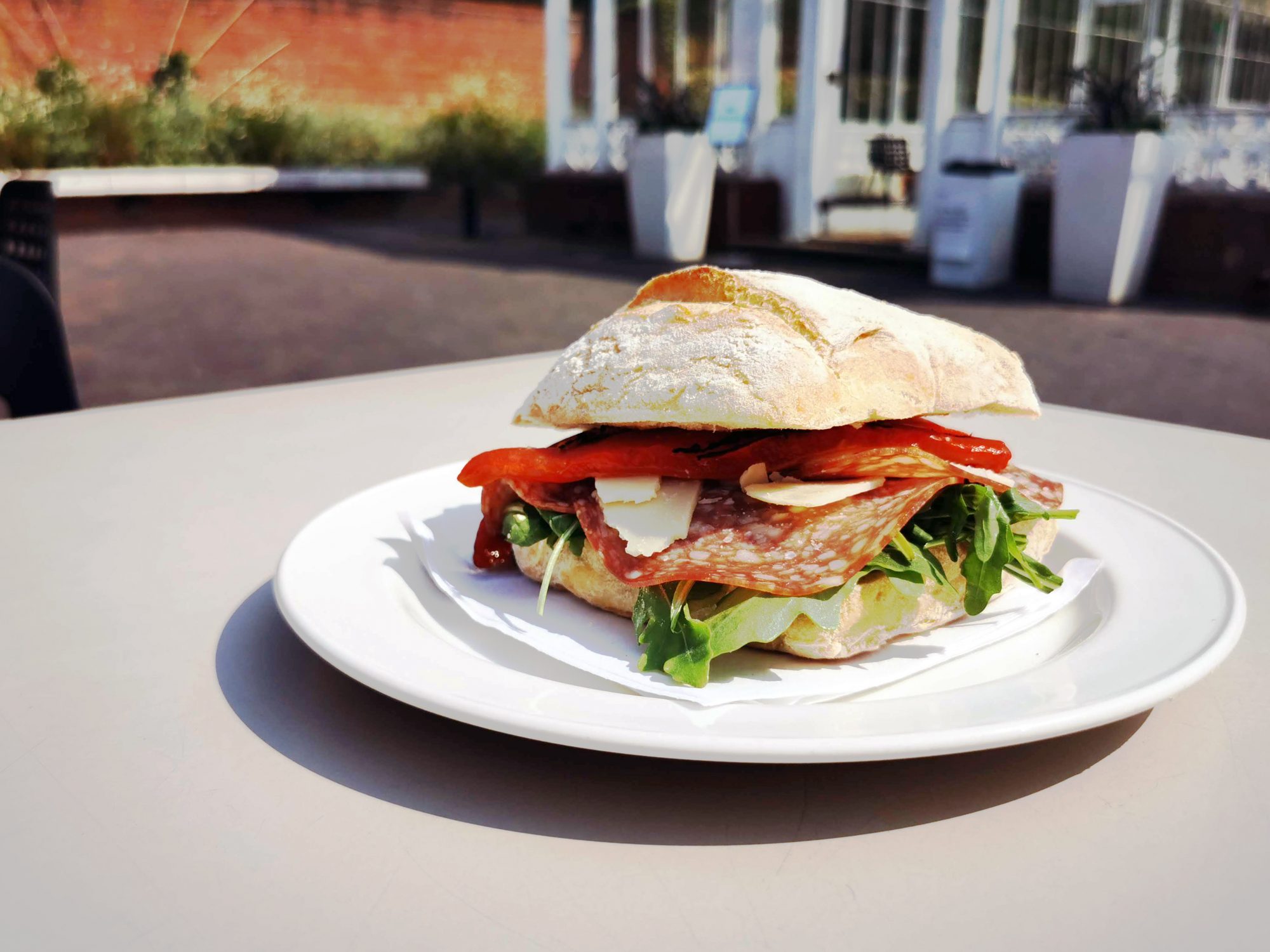 large sandwhich on a plate and table near glass building.