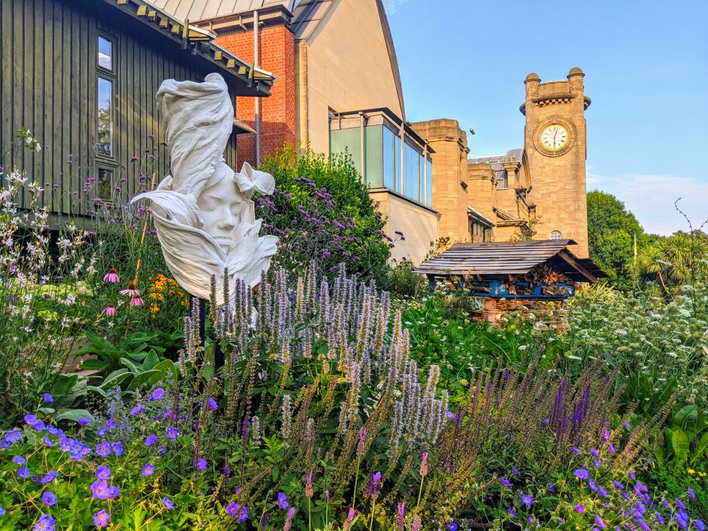 A sculpture rising through flowers in front of the Horniman