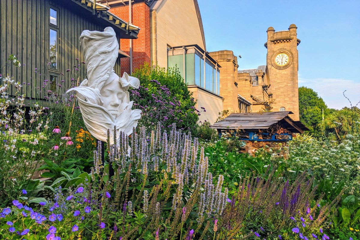 A sculpture rising through flowers in front of the Horniman