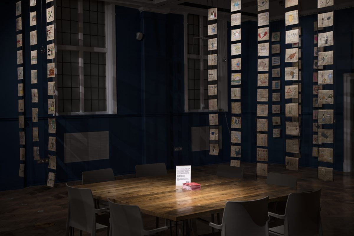 Scrolls hanging from ceiling , with table in center of room, dark lighting