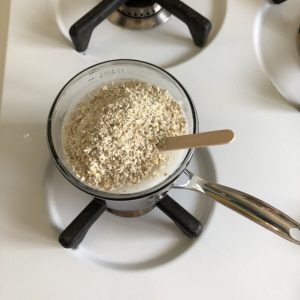 Chopped oats in mixture with wooden stick in saucepan on top of oven