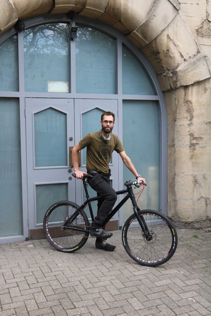 Rich sits on his bike in front of Horniman double doors